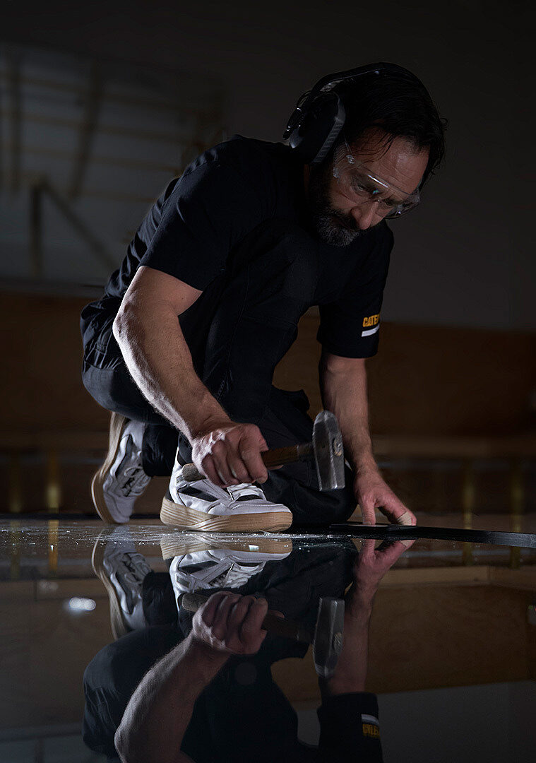 An artist works on a glass panel on the ground using a hammer..