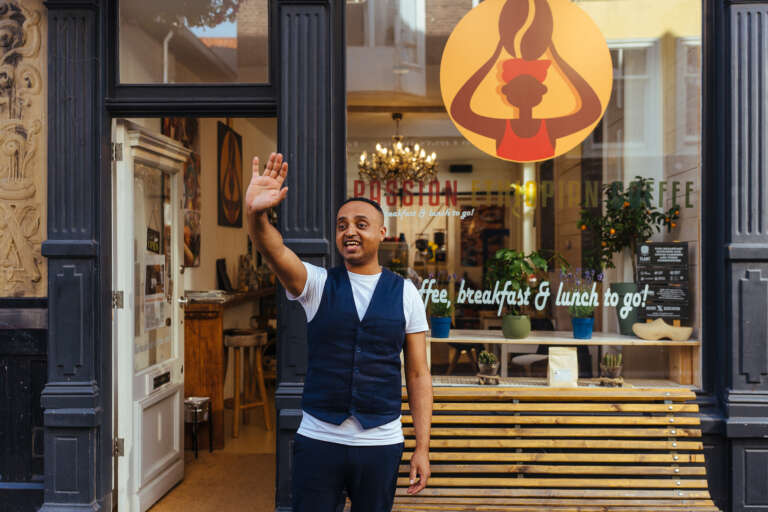 A shop owner greeting people from the entrance of his Ethiopian coffee shop.